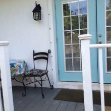 Deck with white railing, small table with chairs, double french doors into bungalow