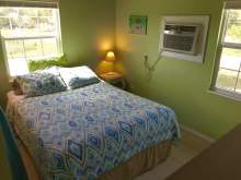 Green wall, double bed with blue and green bedding, lamp, window, wall air conditioning unit