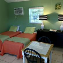 Two twin beds, orange bed spreads, dresser, lamps, wall air conditioning unit, two person table