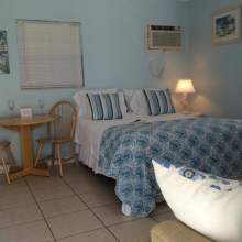 Blue and white bedding on double bed, air conditioning wall unit, window with blinds, two person table